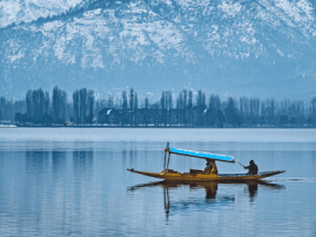 view of a dal lake and a shikara boat in front of snow packed mountains