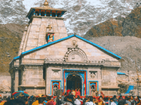 People gather around Kedarnath temple, set against a backdrop of impressive mountains.